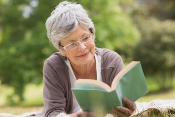 Photo of older lady laying in the grass reading a book