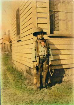 Sepia photo of a young boy in cowboy attire next to a house